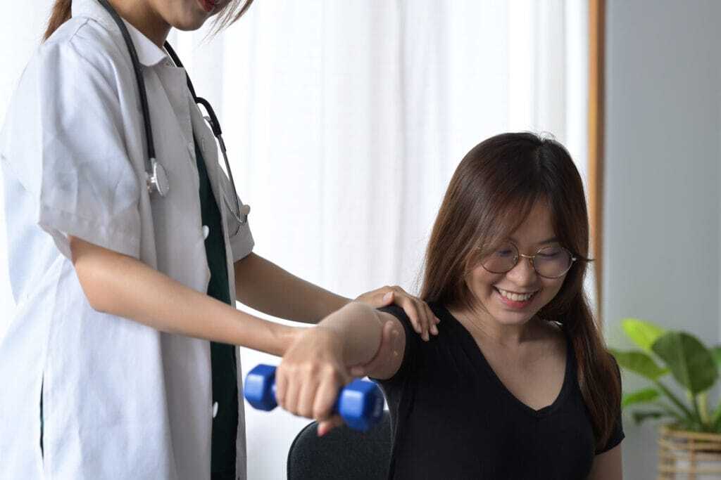 Chiropractor assists patient with arm exercise in Manhattan physical therapy clinic