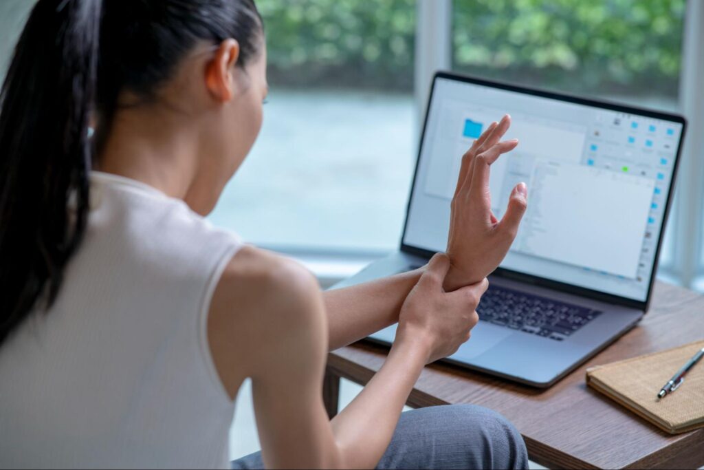 Person holding wrist in pain, seated at a desk with a laptop, suggesting need for chiropractic care in Manhattan, NYC