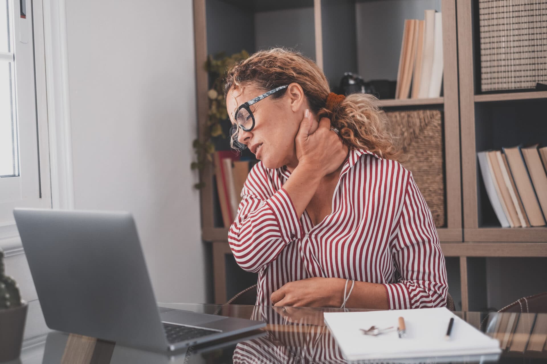Woman holding neck while working on laptop