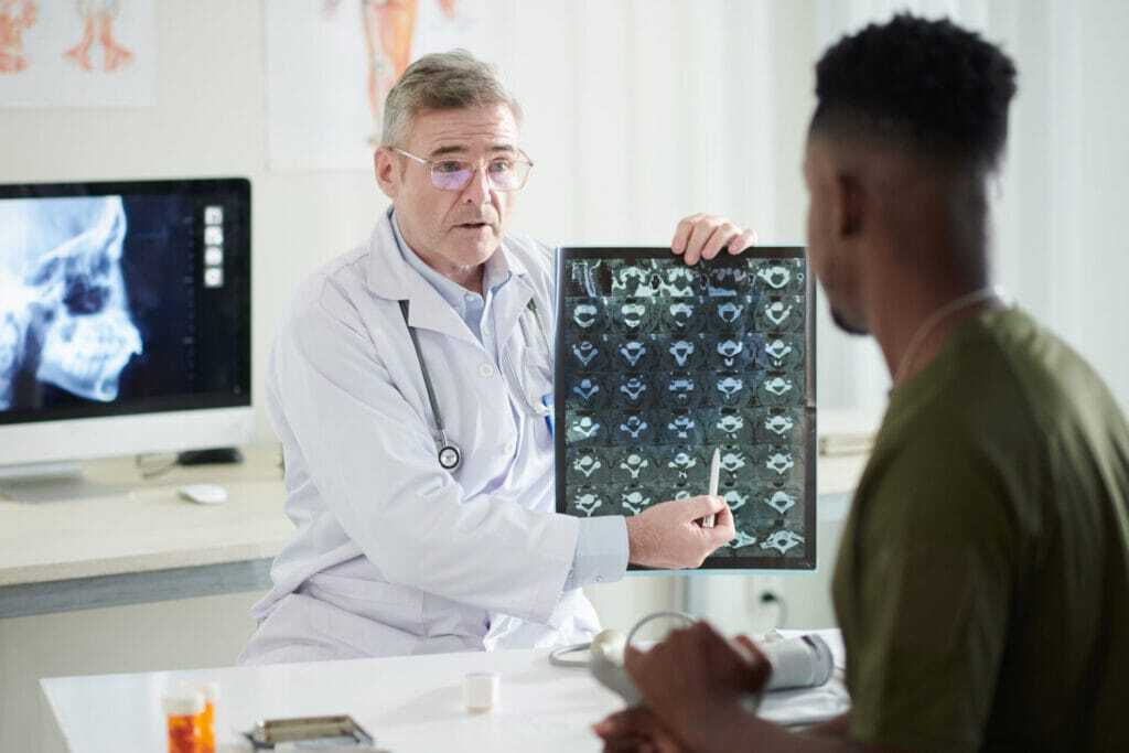 Doctor pointing at spine discs MRI image of military man to show disease progress