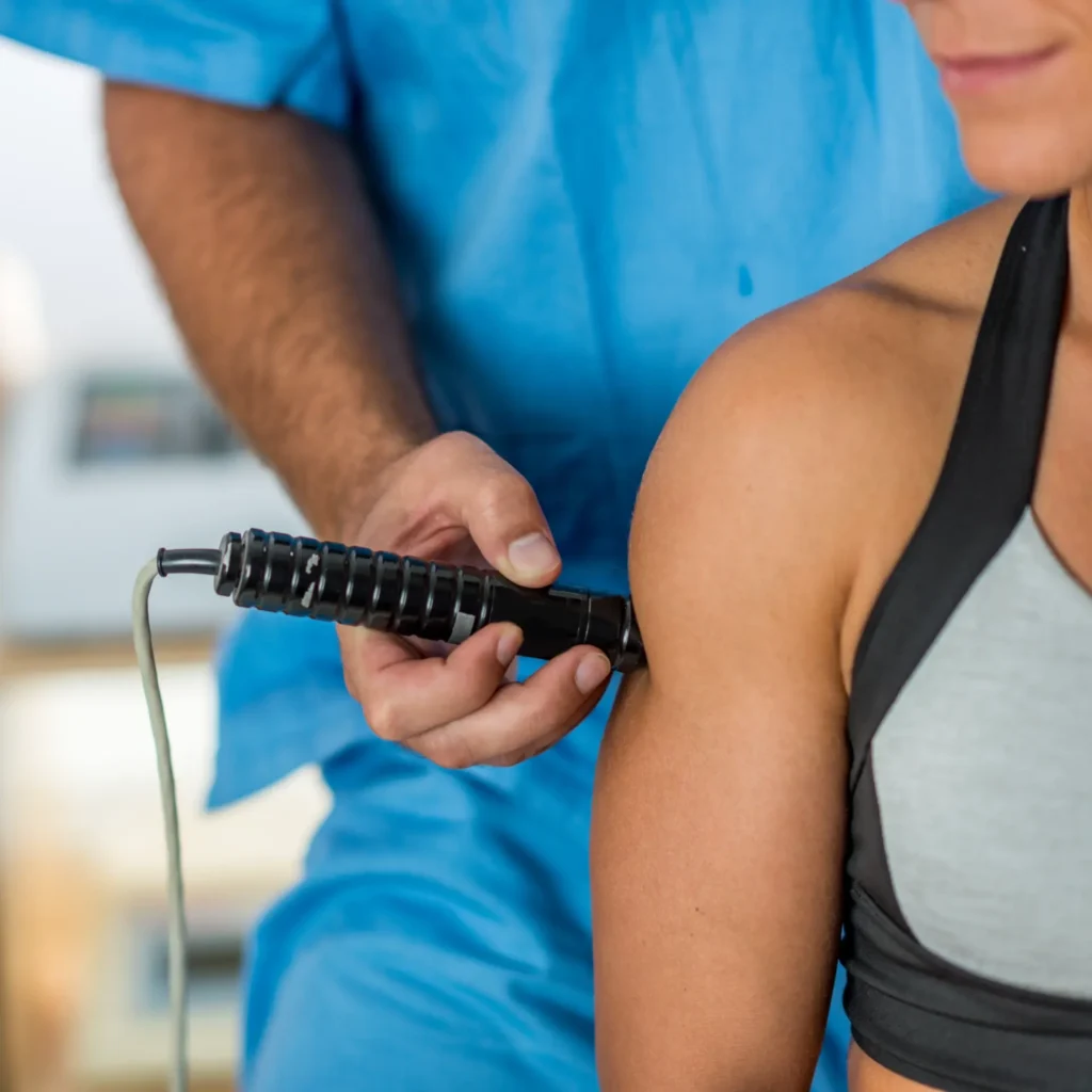 Chiropractor using therapy device on patient's shoulder in Manhattan clinic, NYC