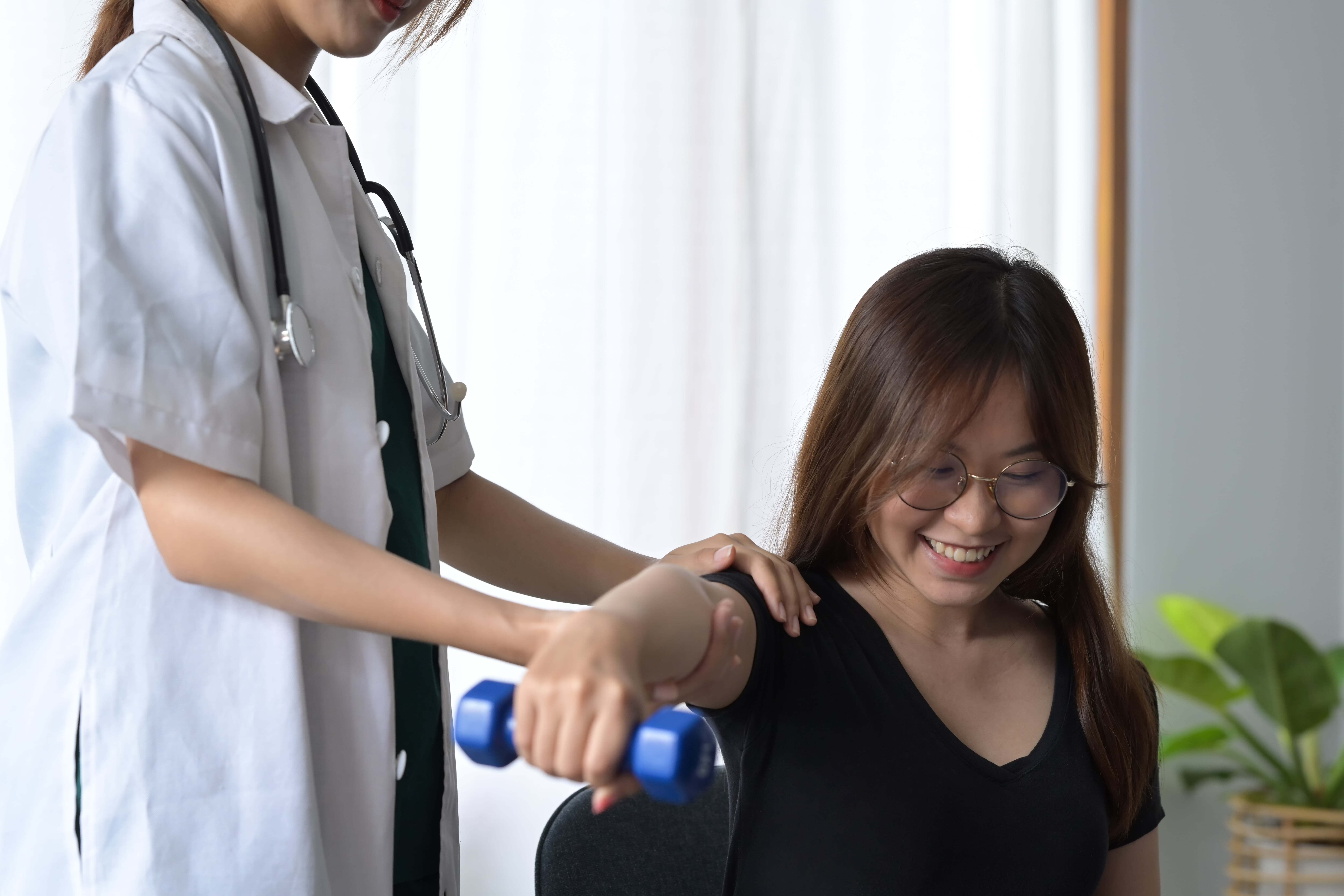 Chiropractor assists patient with arm exercise in Manhattan physical therapy clinic