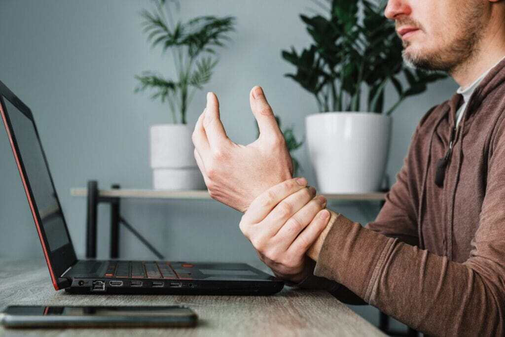 Man holding wrist in pain at desk, suggesting need for chiropractic or physical therapy in Manhattan, NYC