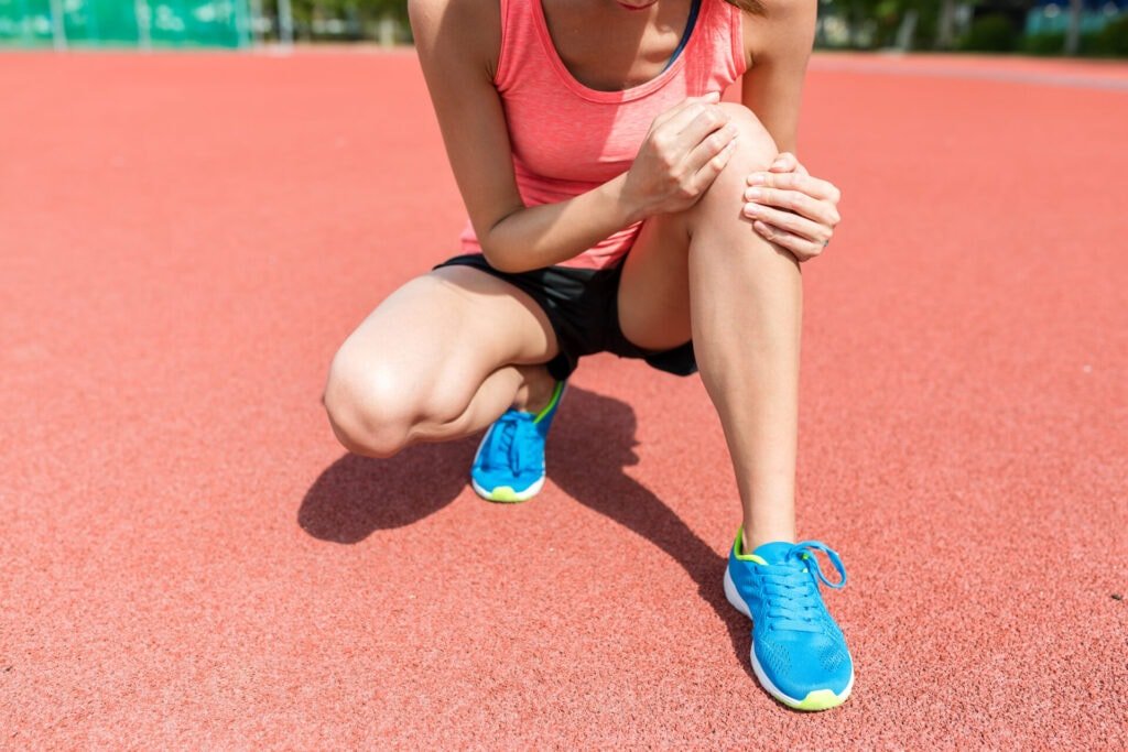 Athlete on track holding knee, highlighting need for chiropractic and physical therapy in Manhattan, NYC