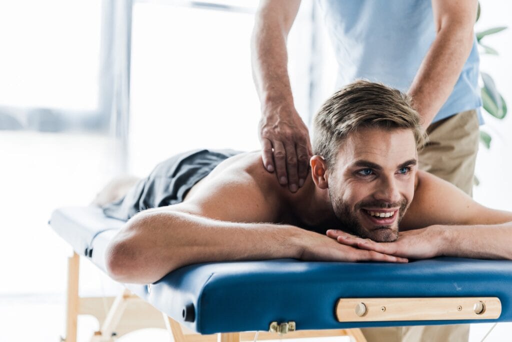 cropped view of chiropractor doing massage to happy patient on massage table