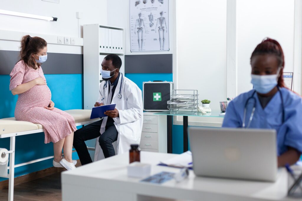 African american medic consulting pregnant woman in cabinet