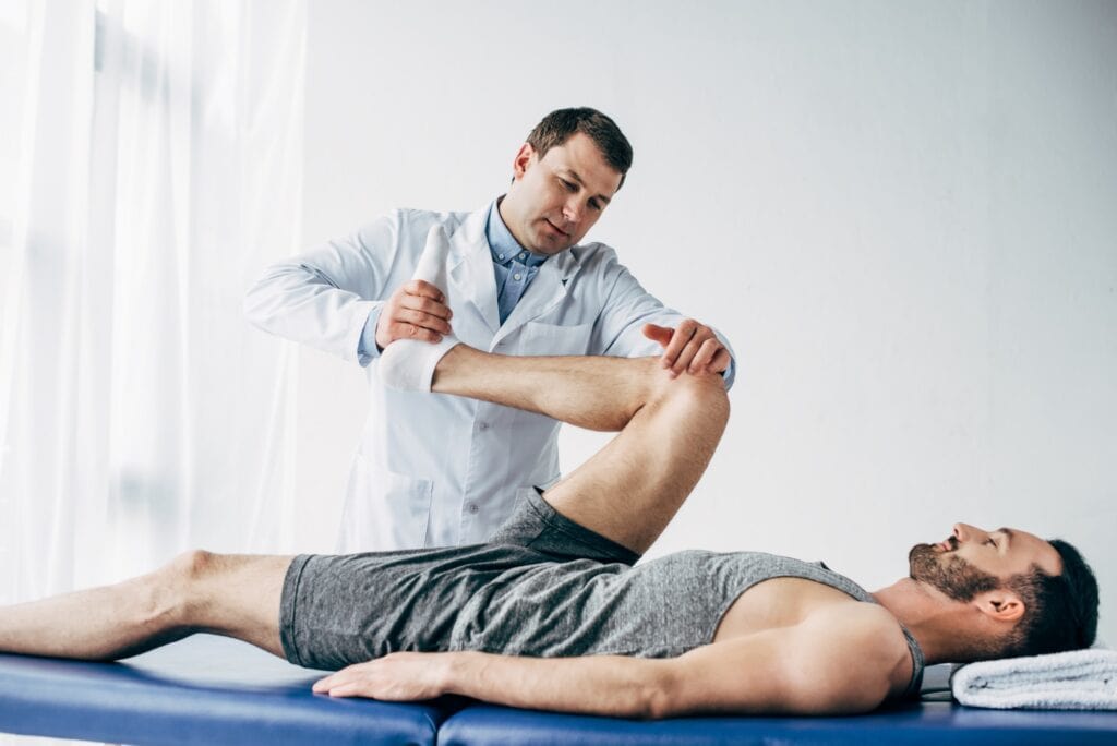 handsome chiropractor stretching leg of patient in hospital