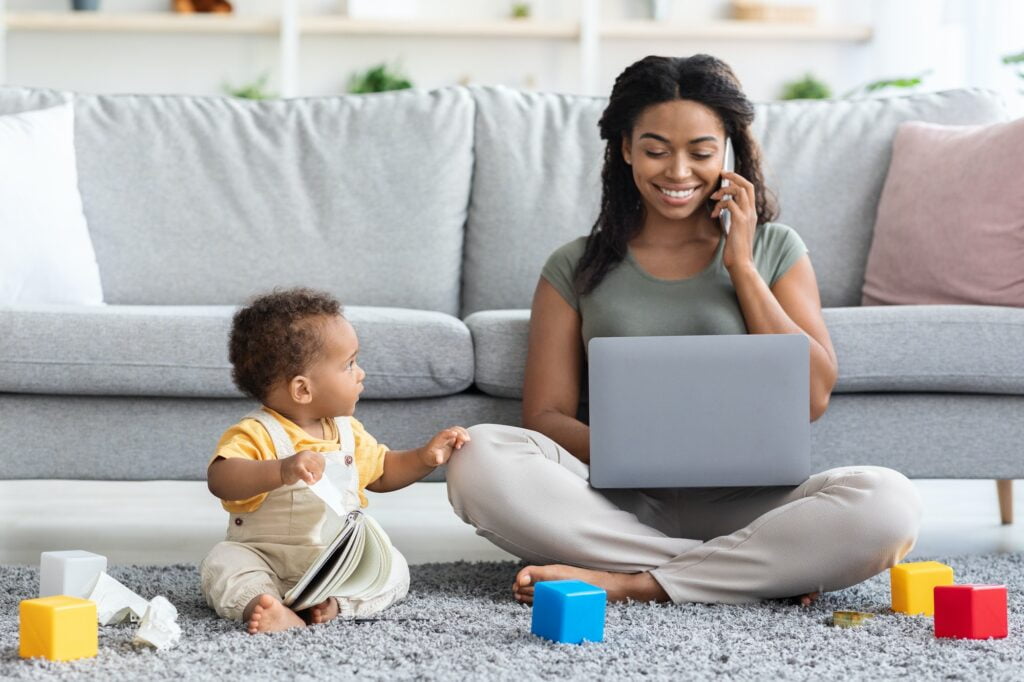 Black Woman Working On Laptop And Taking Care Of Her Infant Child