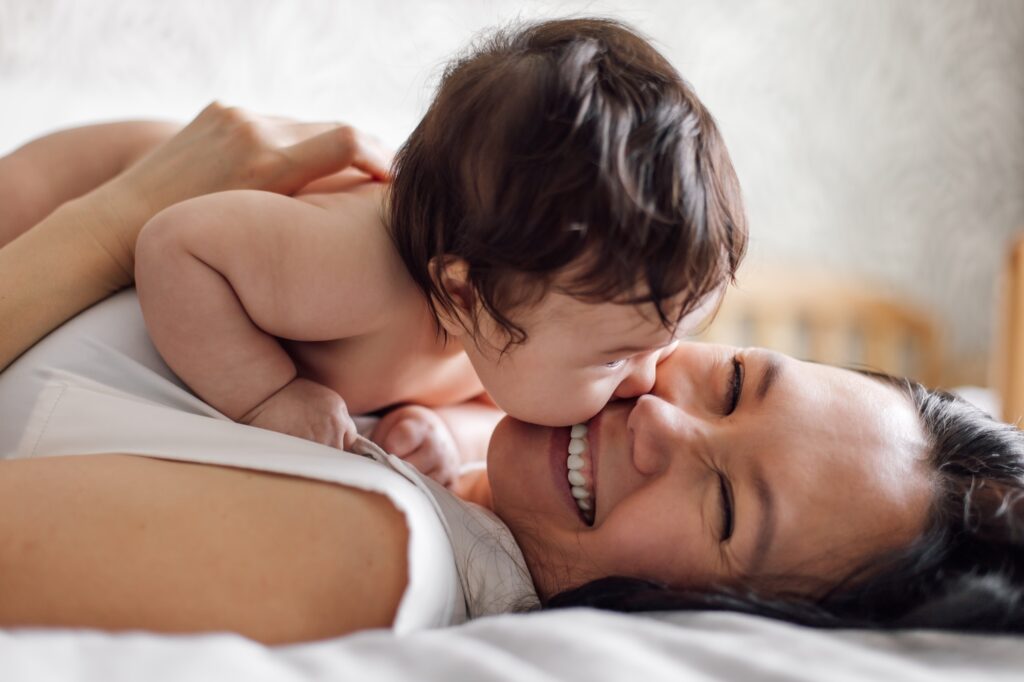 Closeup portrait of happy young mother and infant girl lying on bed in room. Carefully hold naked