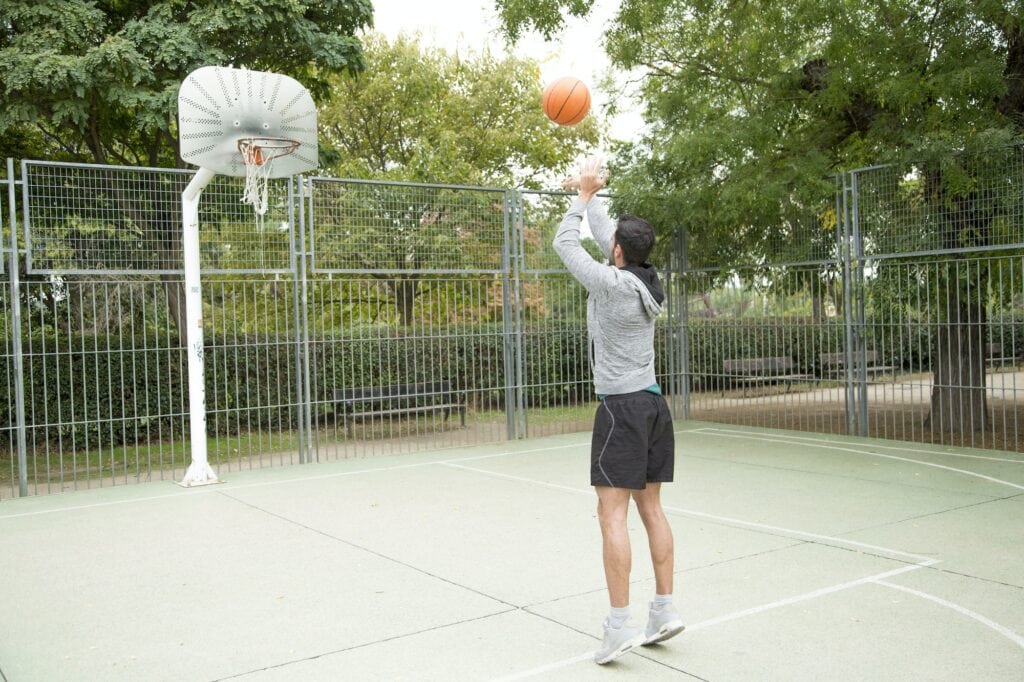 Man throwing a ball on an outdoor basketball court.