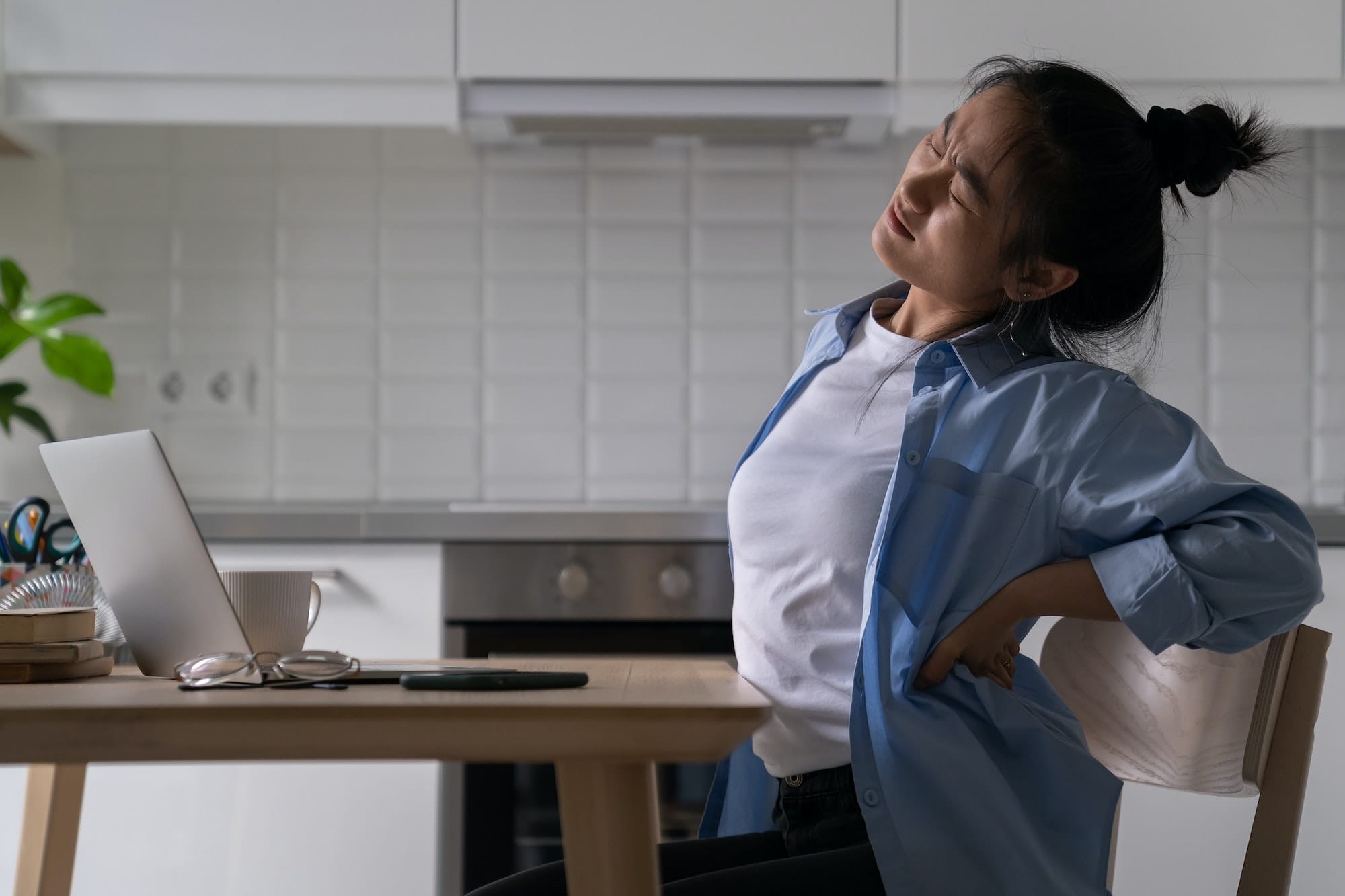 Unhappy Asian student girl suffering from lower back pain while studying from home