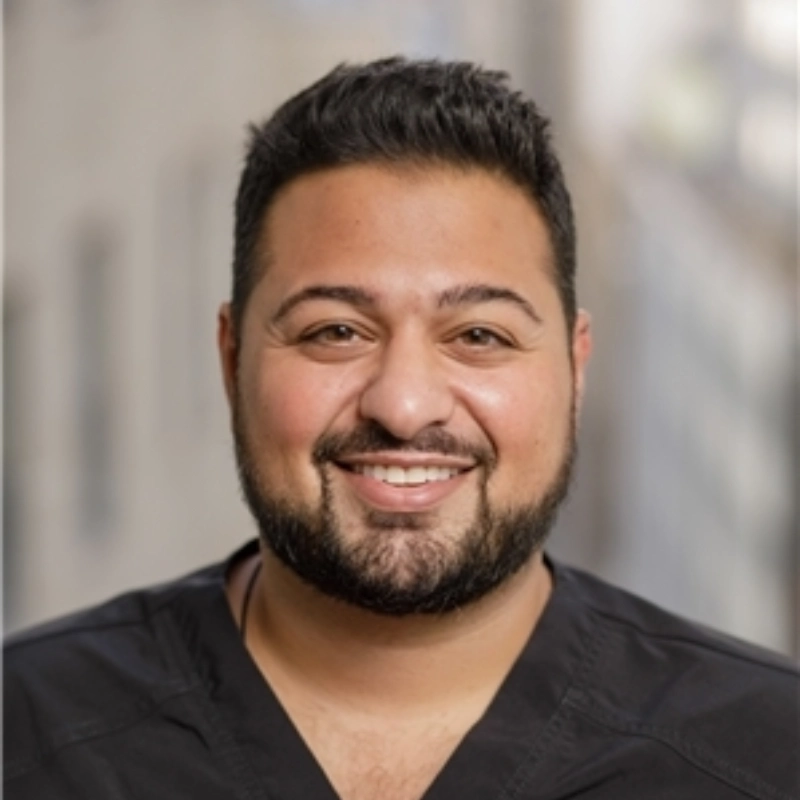 A male chiropractor in scrubs smiling and looking at the camera