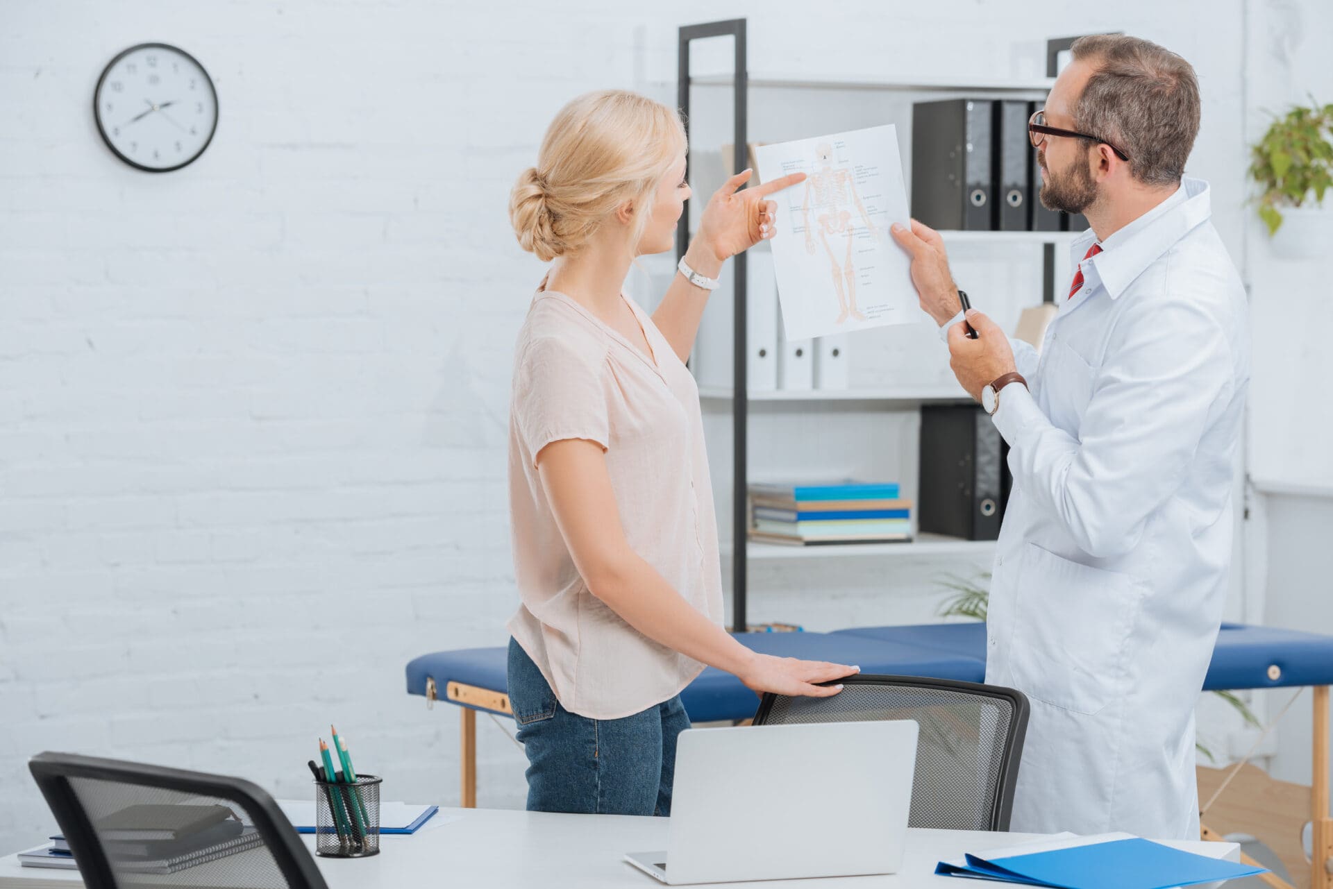 chiropractor in white coat showing human body scheme to female patient in hospital