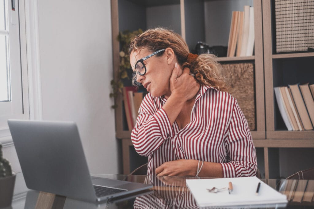 "Woman in striped shirt feeling neck pain while working on laptop, possible pinched nerve."